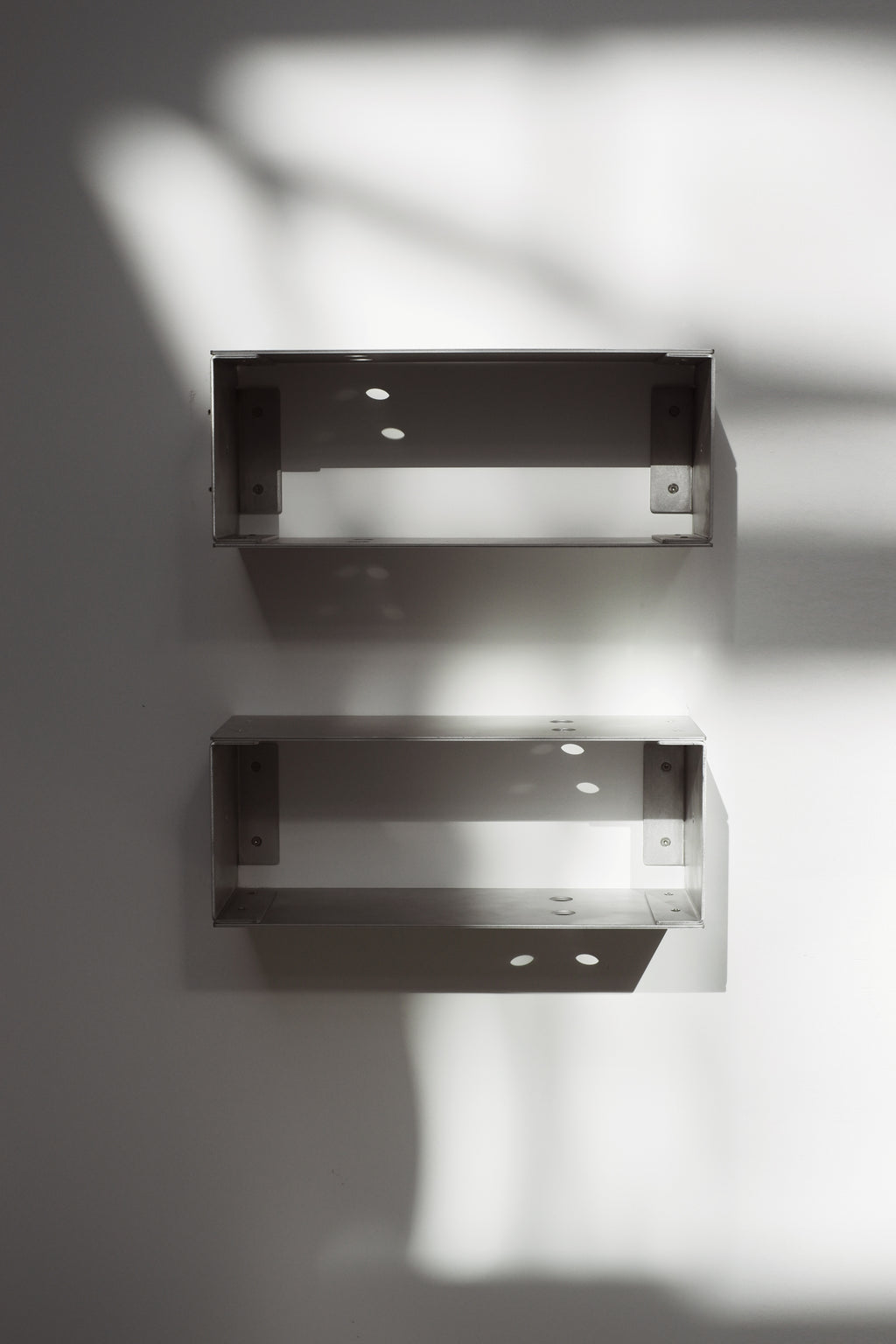 Two metallic wall shelves on a white wall with soft shadows.
