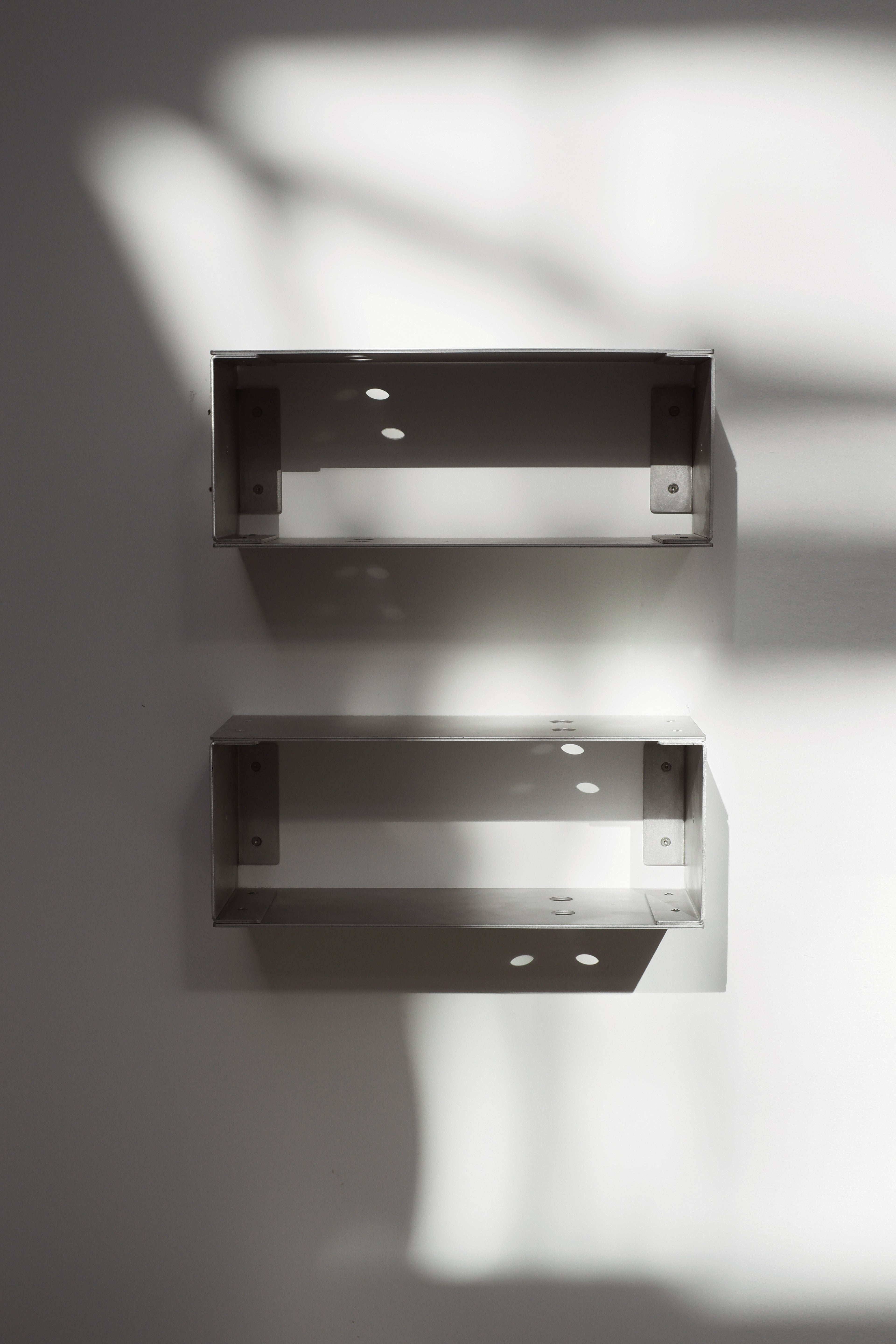 Two metallic wall shelves on a white wall with soft shadows.