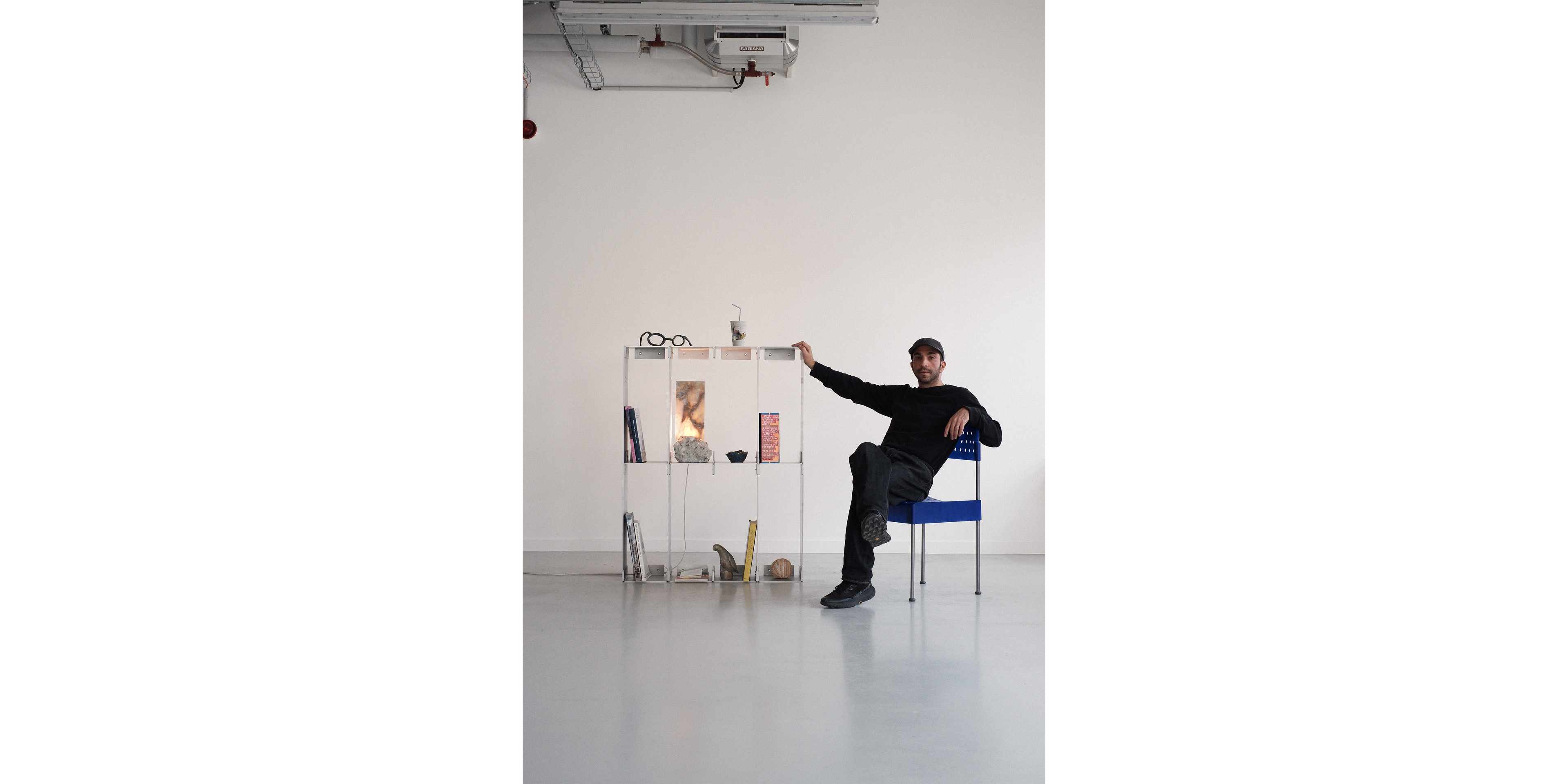 Person sitting on a chair in a minimalistic room with a white wall and gray floor.