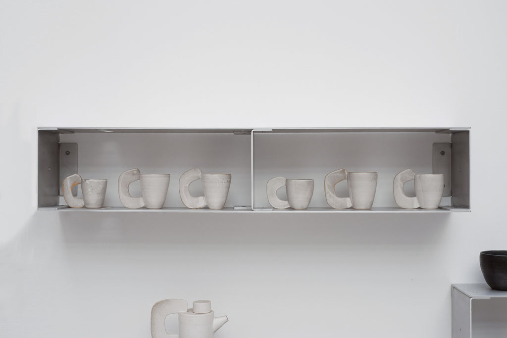 Row of white ceramic cups on a shelf against a white wall