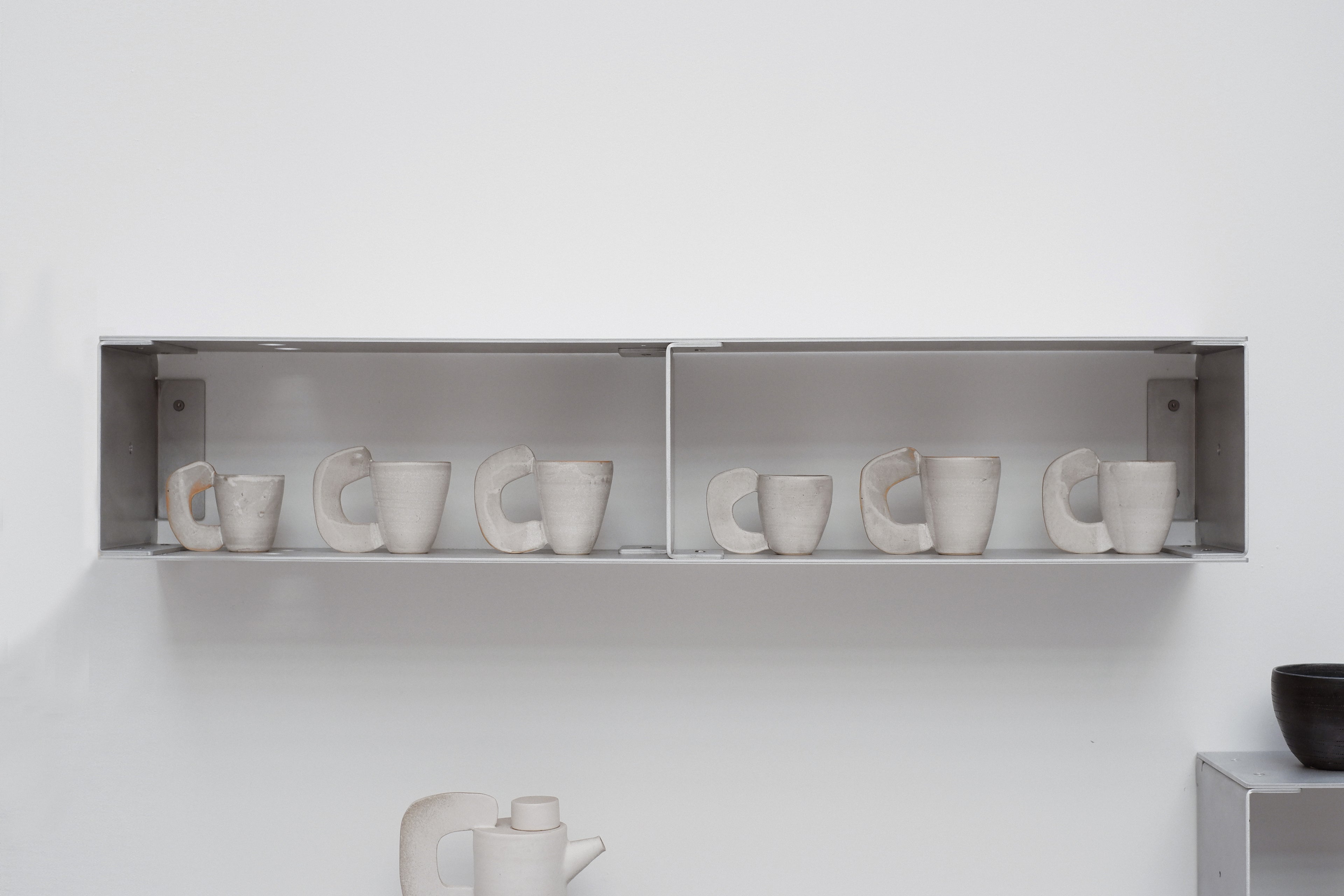 Row of white ceramic cups on a shelf against a white wall