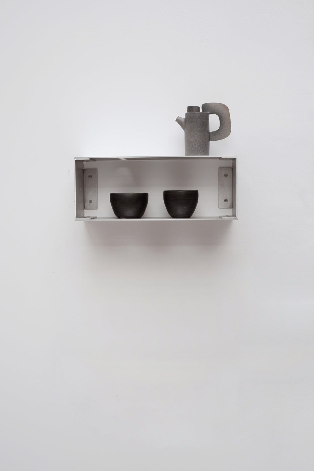 Metal shelf with two black cups and a gray teapot on a white wall