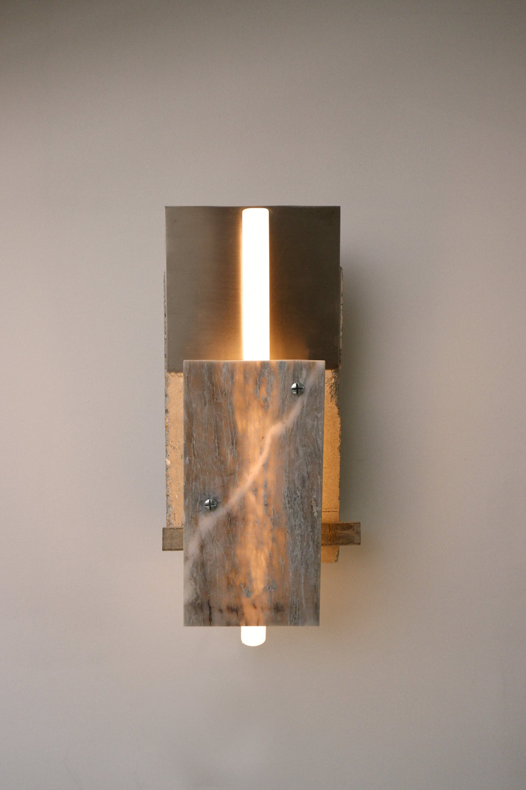 A wall-mounted lamp featuring a concrete structure with a marble and stainless steel finish, emitting a warm glow.